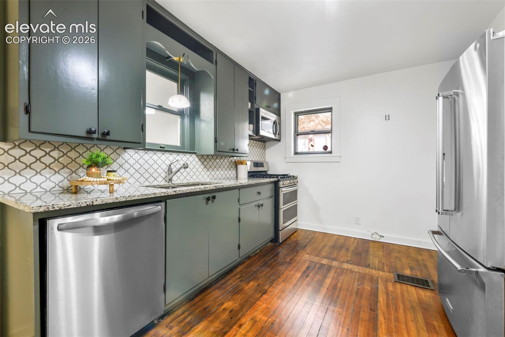 Kitchen featuring painted cabinetry, stone-finish countertops, patterned tile backsplash, stainless steel appliances, and wood-finish flooring