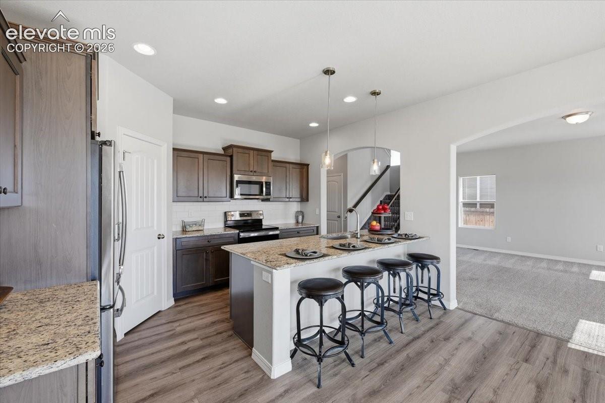 Kitchen featuring stained wood cabinetry, stone countertops, stainless steel appliances, a center island with pendant lighting, and wood-finish flooring