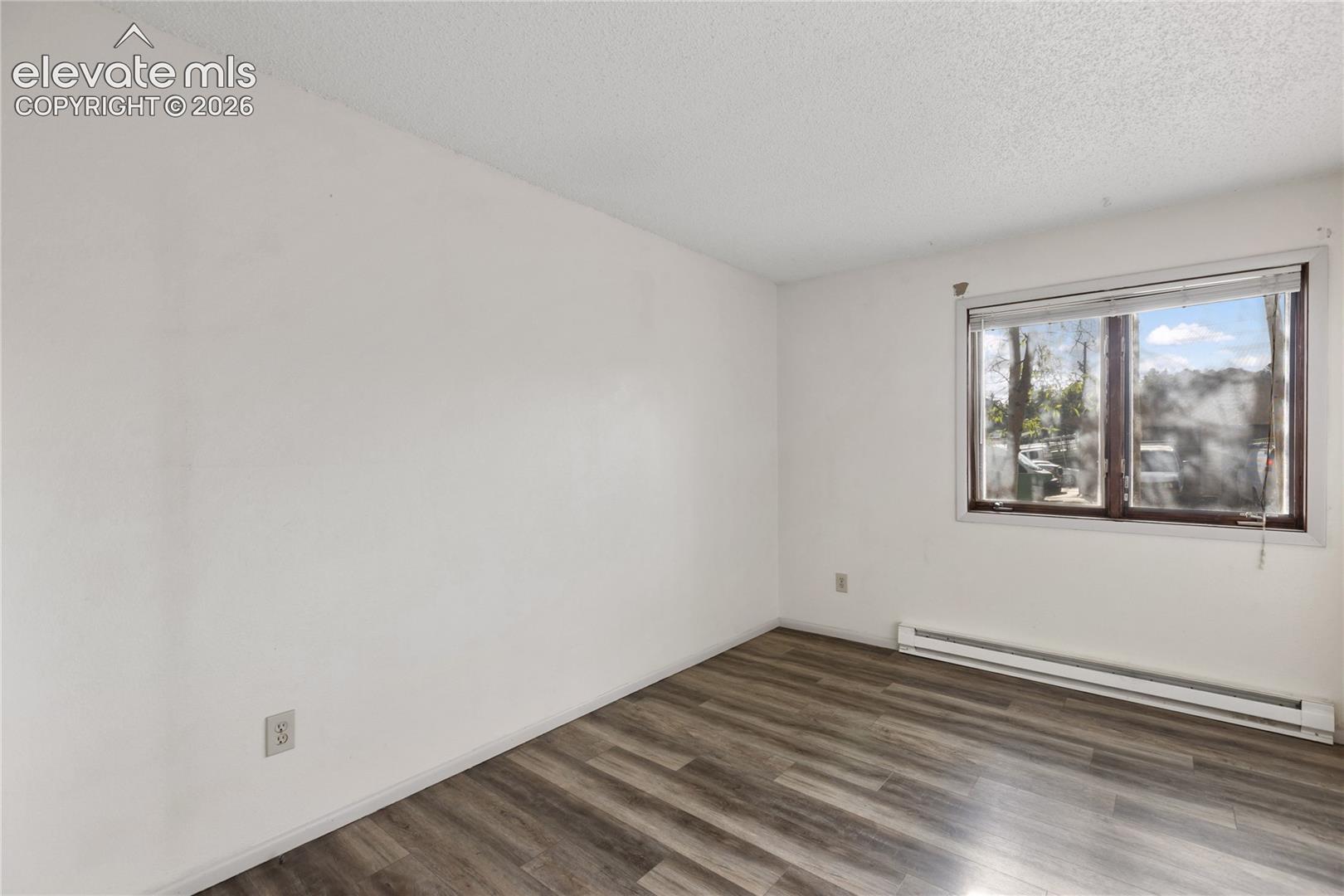 Room featuring wood-finish flooring, white walls, a single window, and a baseboard heater