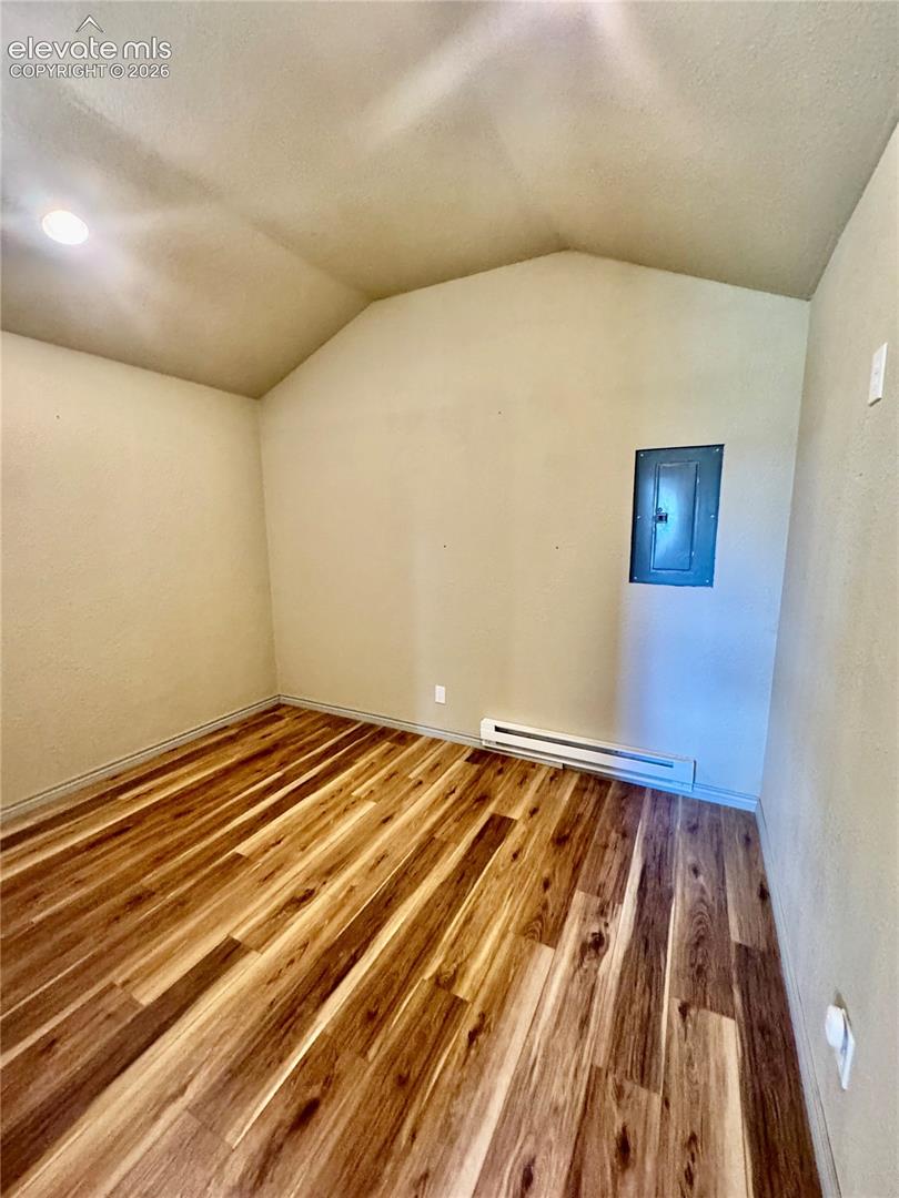 Vaulted ceiling with recessed lighting, wood-finish flooring, and white wall finishes