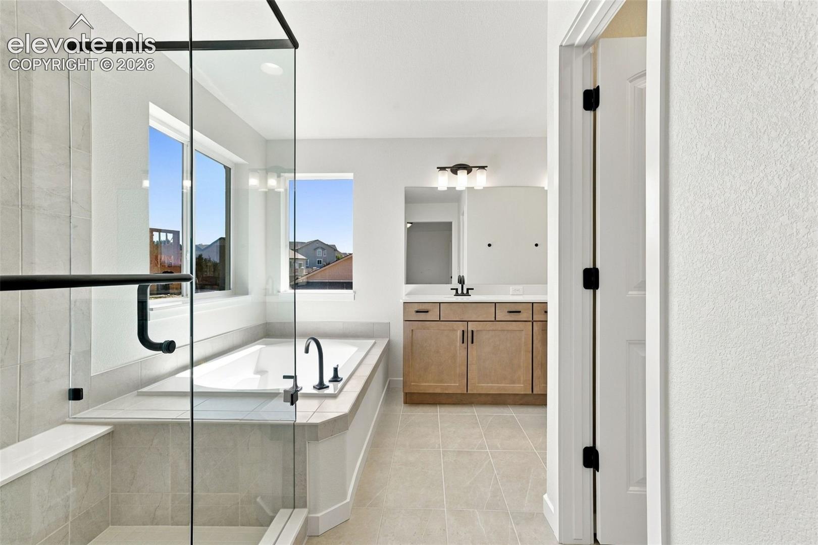 Glass-enclosed shower with matte black hardware, built-in soaking tub with matte black faucet, and double vanity with quartz countertop.