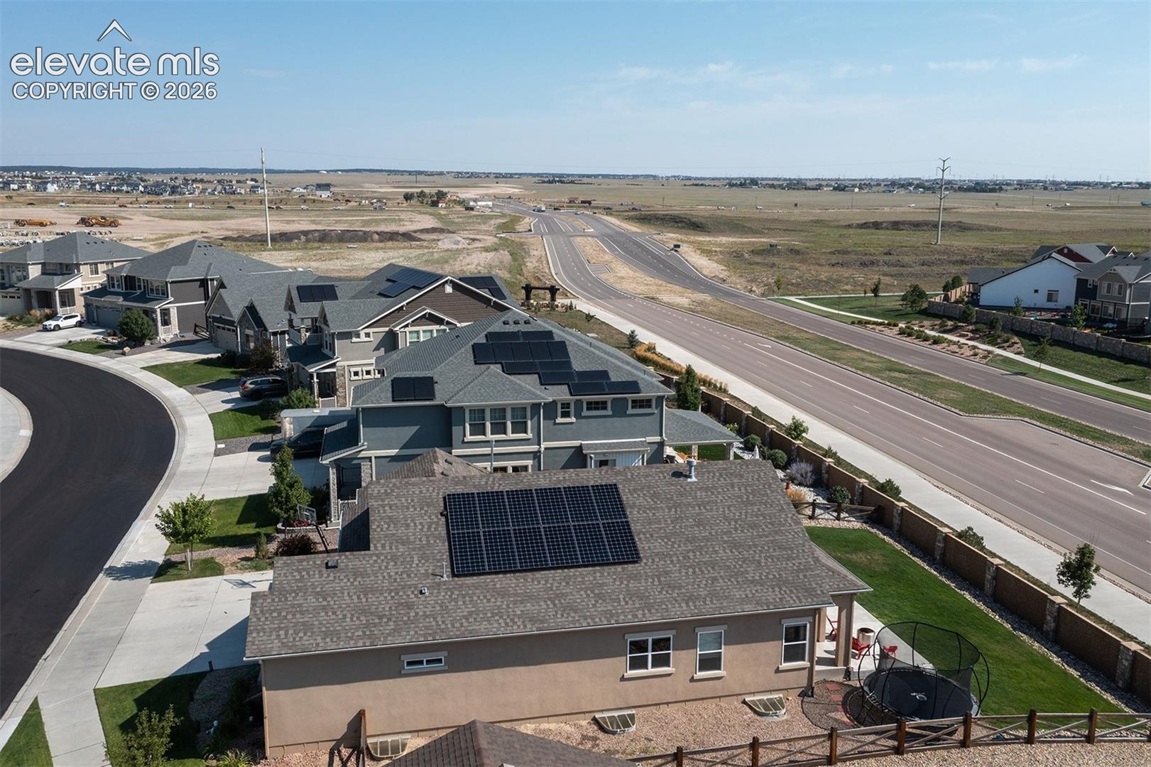 Asphalt shingle roof with solar panels, stucco exterior, rear patio with paved surface, and fenced property perimeter