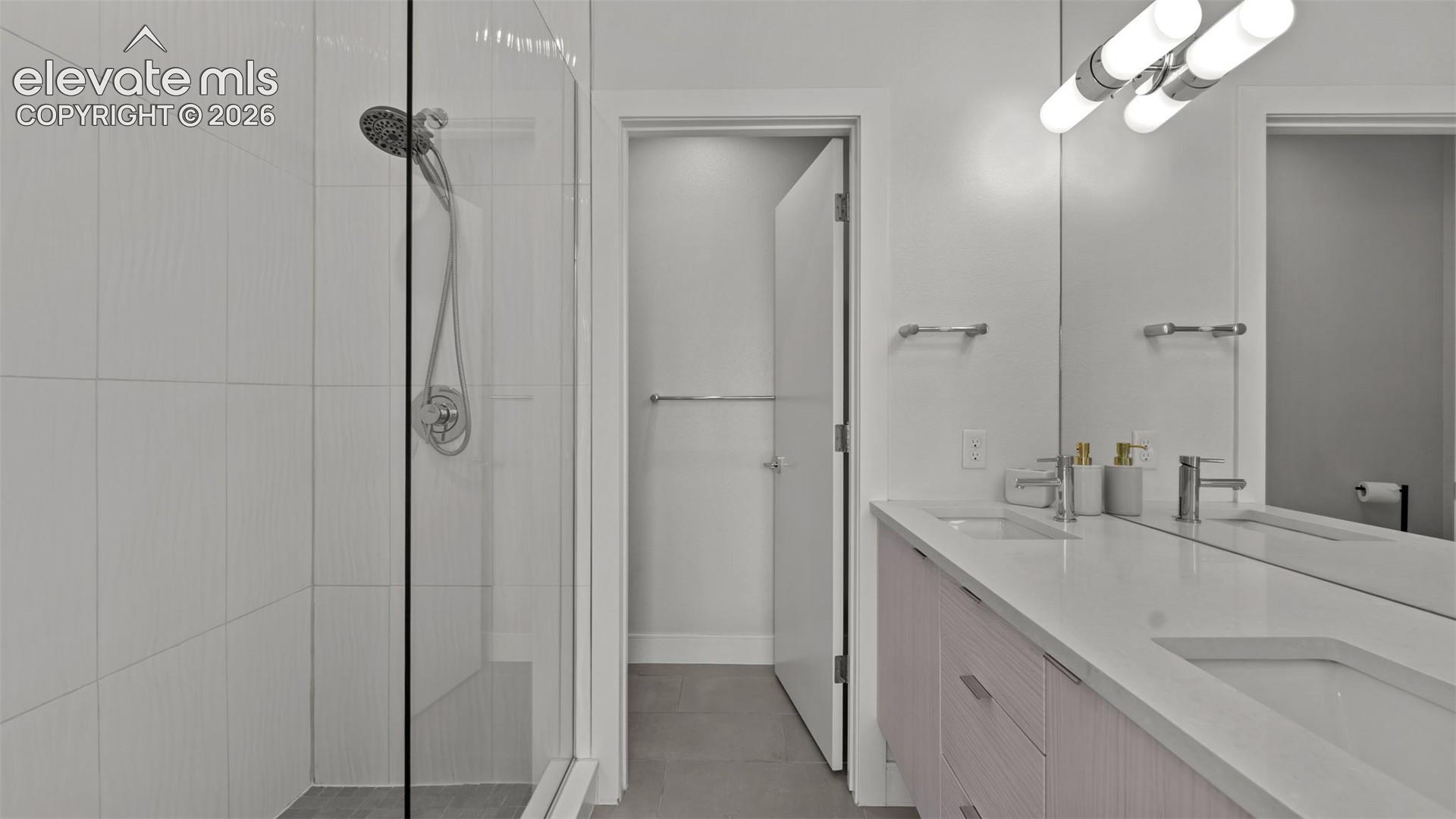 Floating vanity with dual rectangular undermount sinks, quartz countertops, glass-enclosed shower, wall-mounted light fixtures, and large-format wall tiling