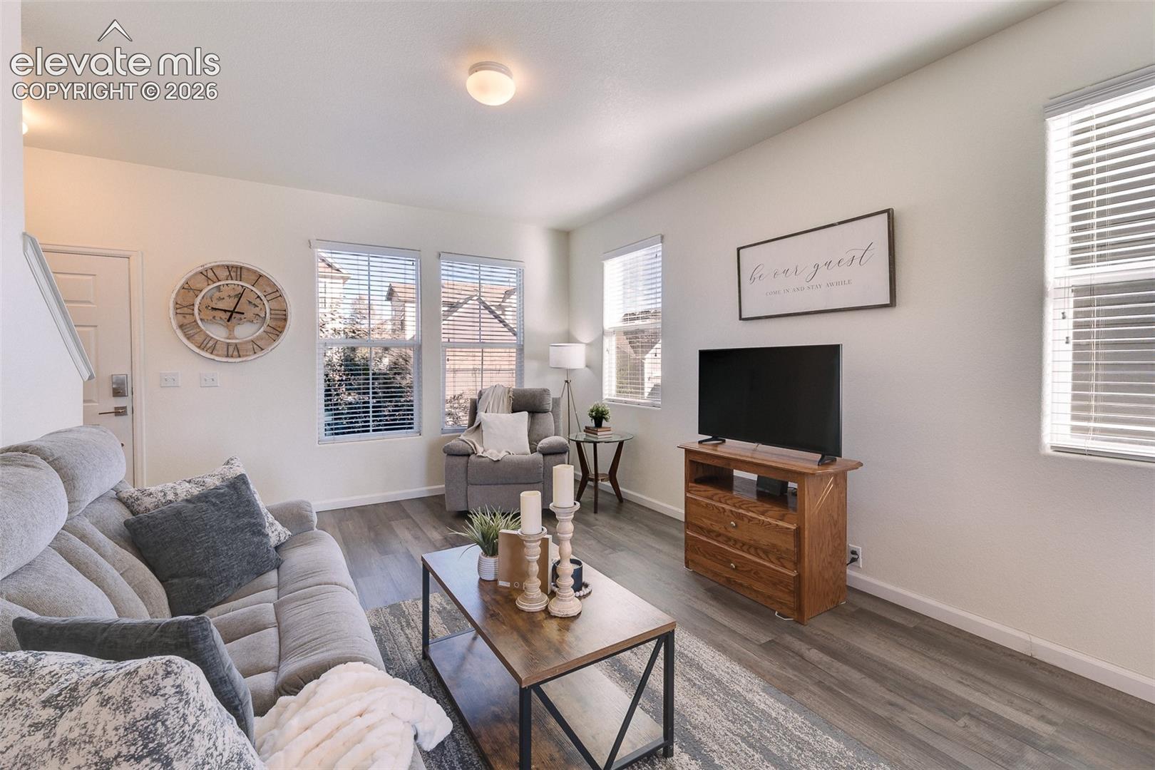 Wood-finish flooring, multiple windows with horizontal blinds, and a wood media console