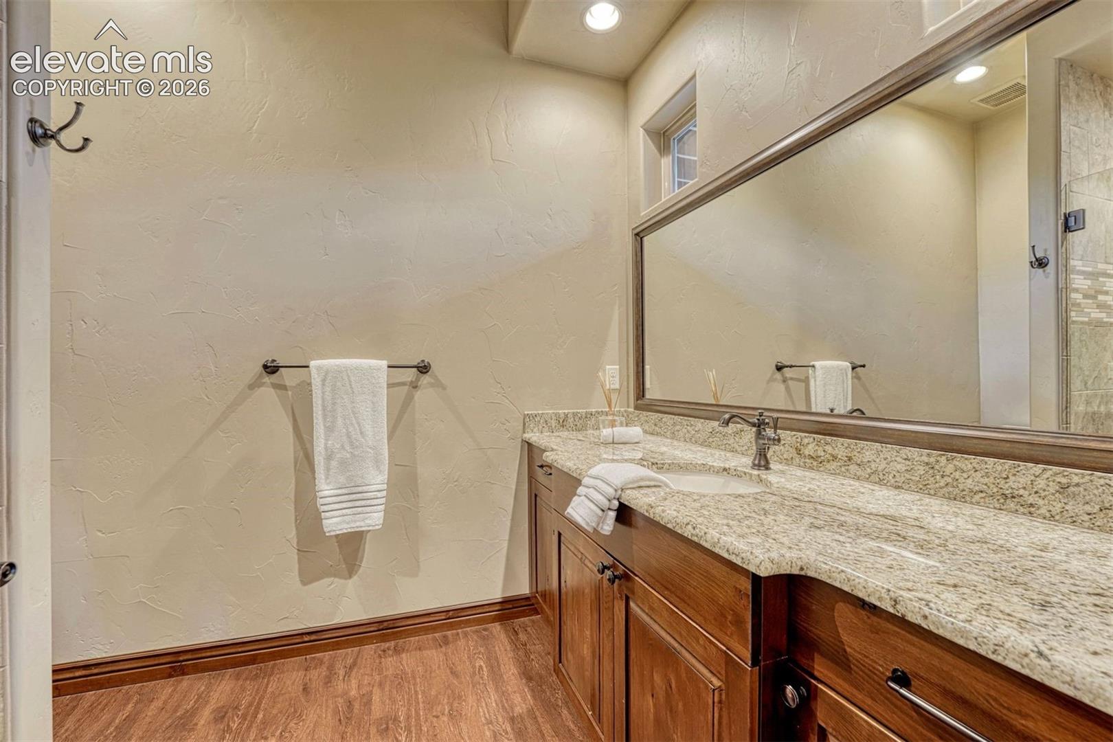 Dual vanity with undermount sinks, granite countertop, wood-finish flooring, and a large framed mirror