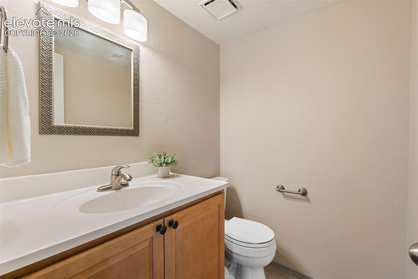 Bathroom featuring a wood-finish vanity with a white countertop and oval sink, brushed metal faucet, framed wall mirror, and three-light overhead fixture