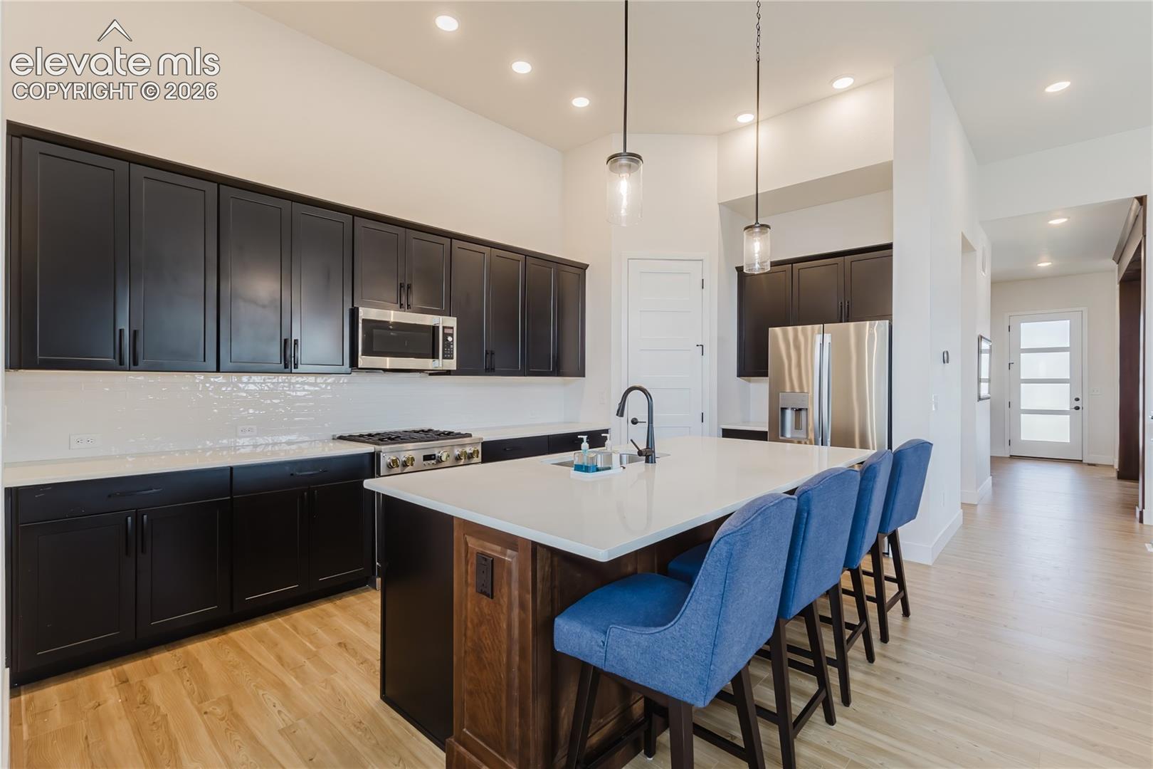 Kitchen featuring dark cabinetry, stainless steel appliances, a 4' X 8' center island with sink and  white solid countertops