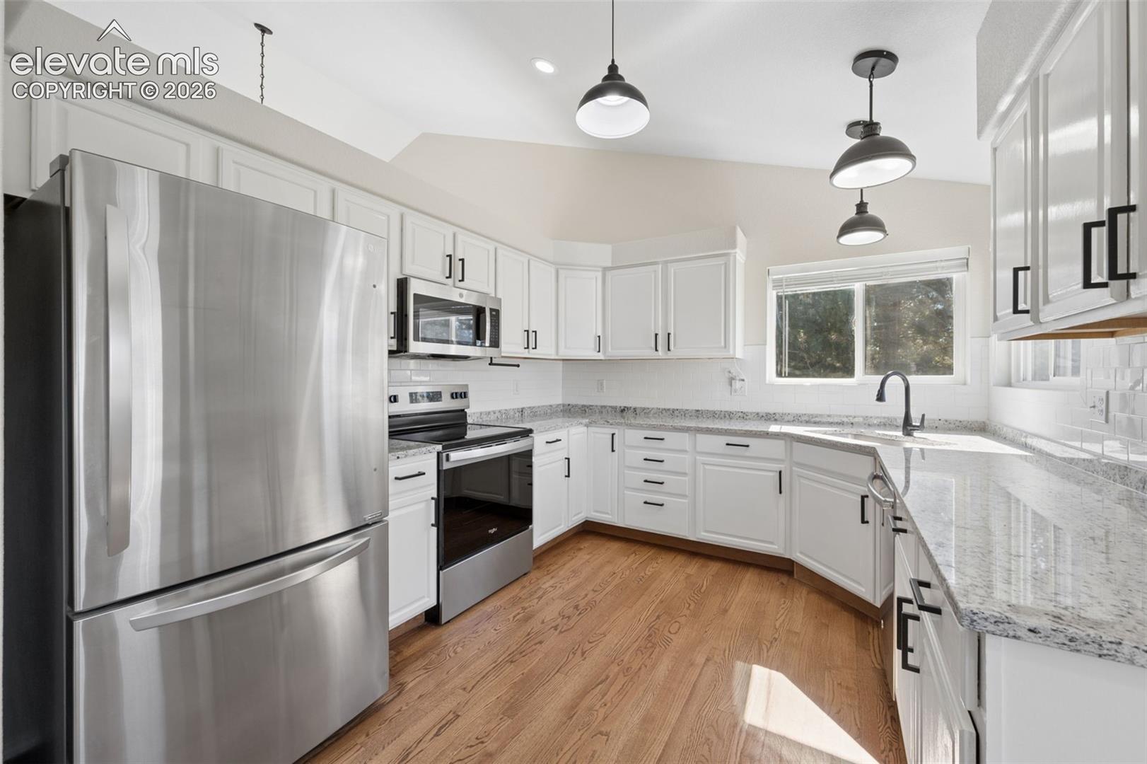 Kitchen featuring white cabinetry, stone countertops, stainless steel appliances, wood-finish flooring, and pendant lighting