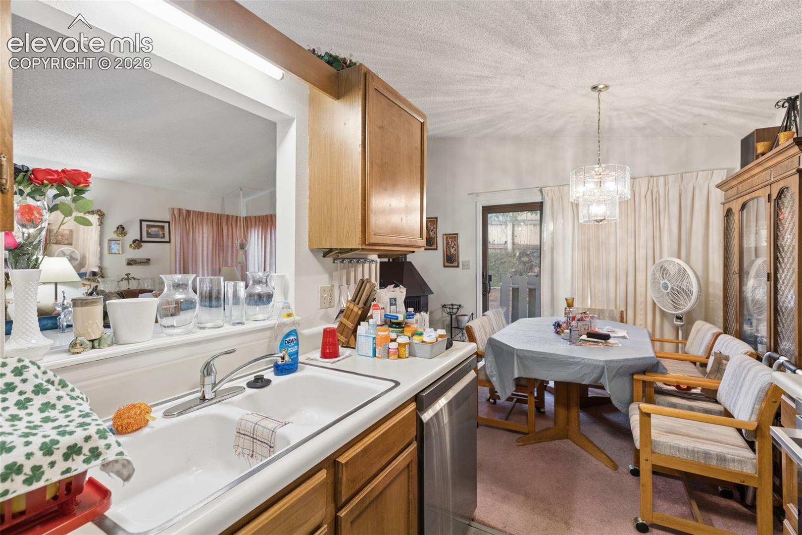 Kitchen featuring wood cabinetry, stainless steel dishwasher, double-basin sink with a chrome faucet, and a pass-through opening