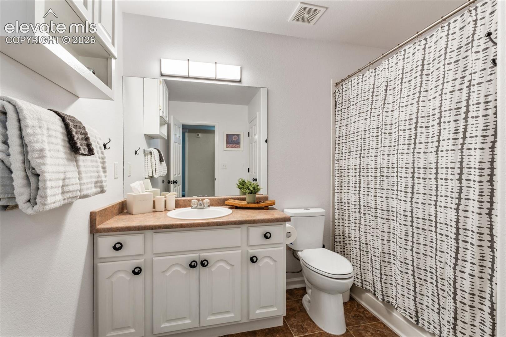 Bathroom featuring a white vanity cabinet with decorative paneling, neutral-tone solid surface countertop, inset sink, large wall-mounted mirror, and tile flooring