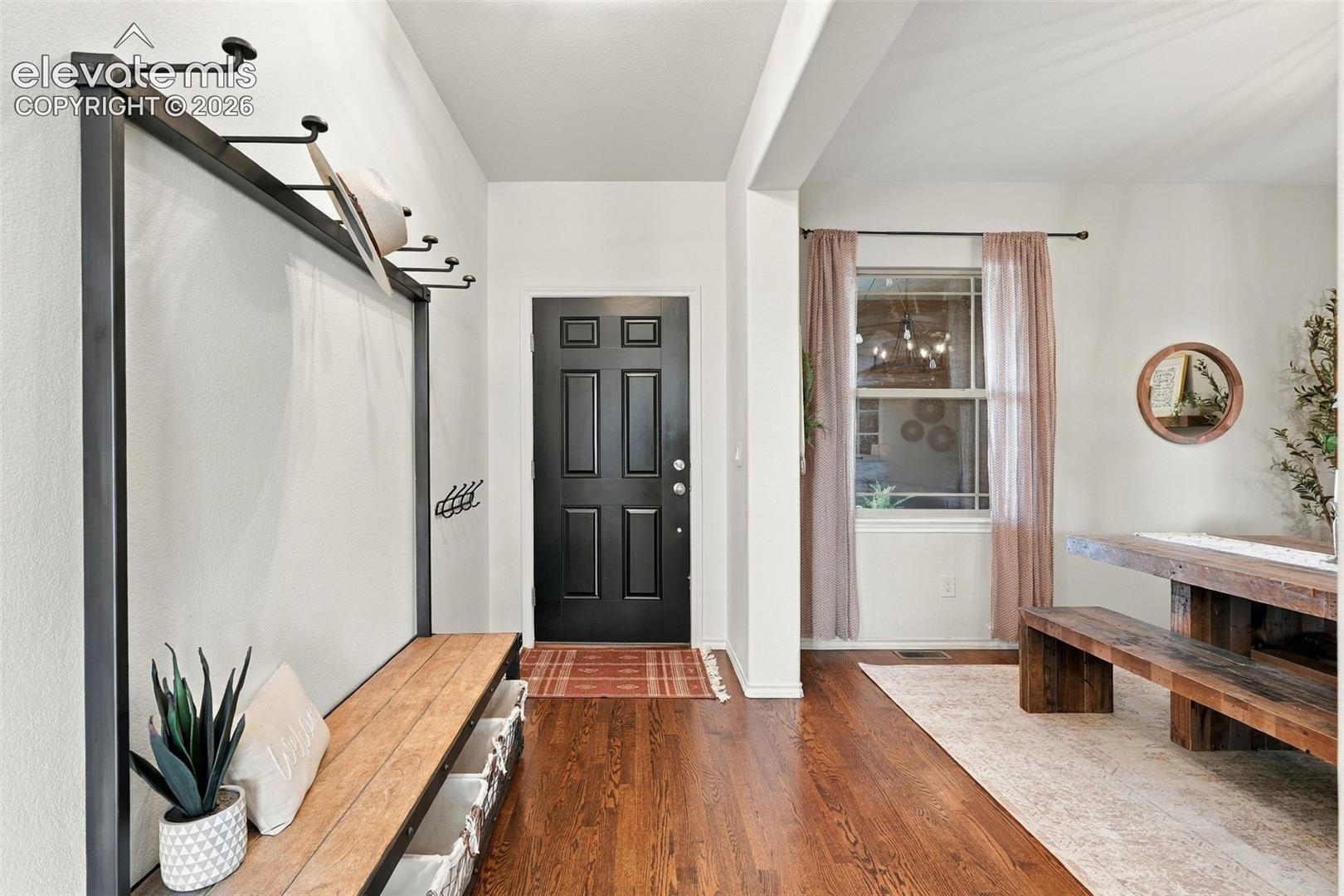 Entryway featuring dark-stained wood flooring, a black six-panel entry door, and a built-in metal-framed bench with integrated wall-mounted hooks