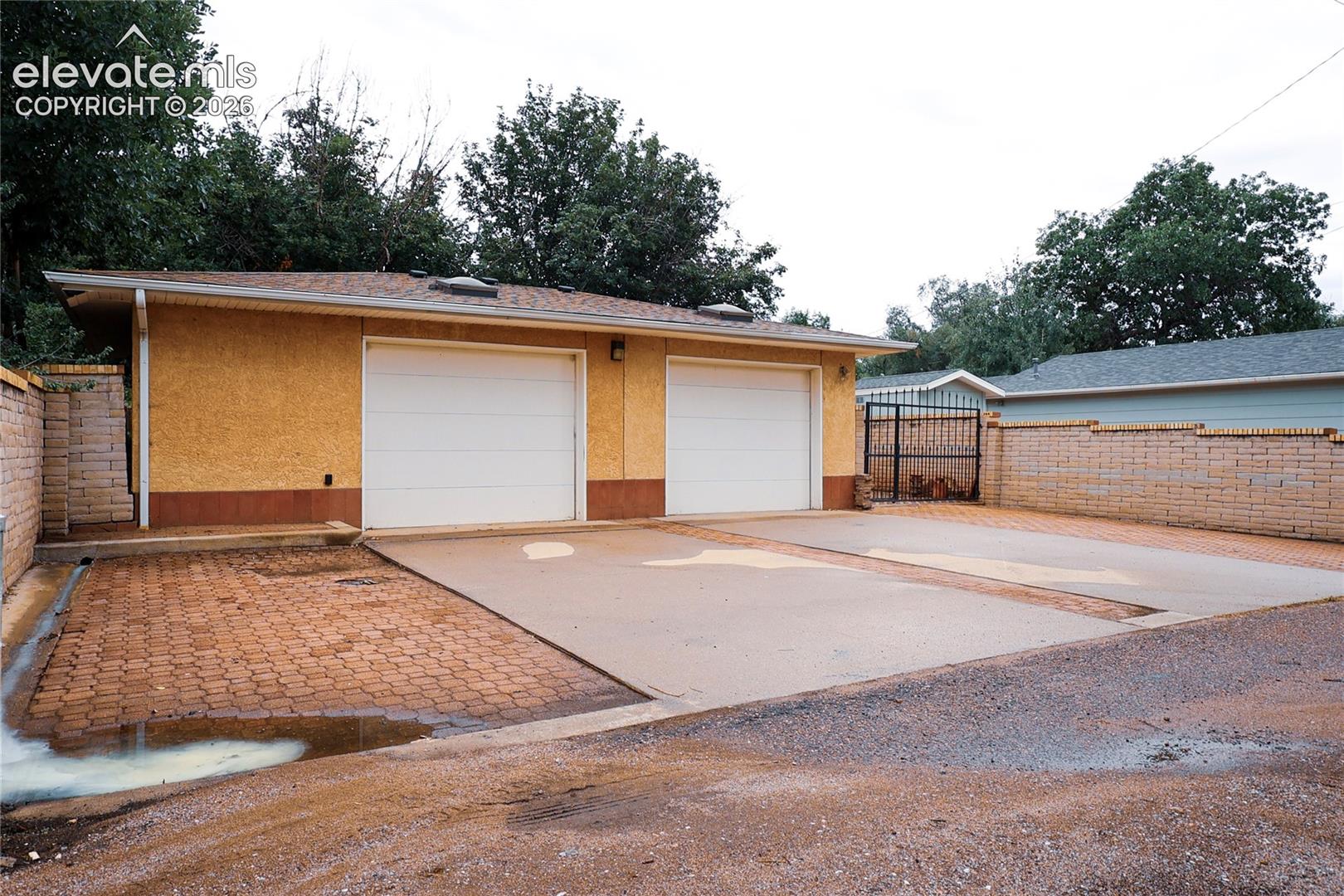 Spacious driveway with herringbone brick paving and concrete apron, complemented by a modern garage featuring two white panel doors
