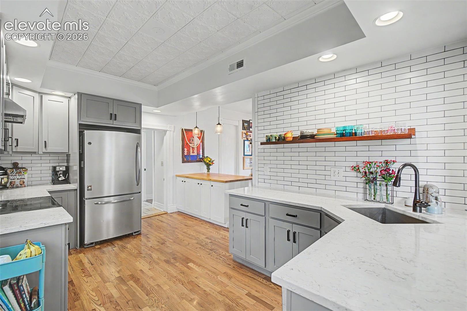 Updated kitchen featuring light gray cabinetry, white tile backsplash, stainless steel appliances, a wood-finish breakfast bar/ kitchen island, and hardwood flooring