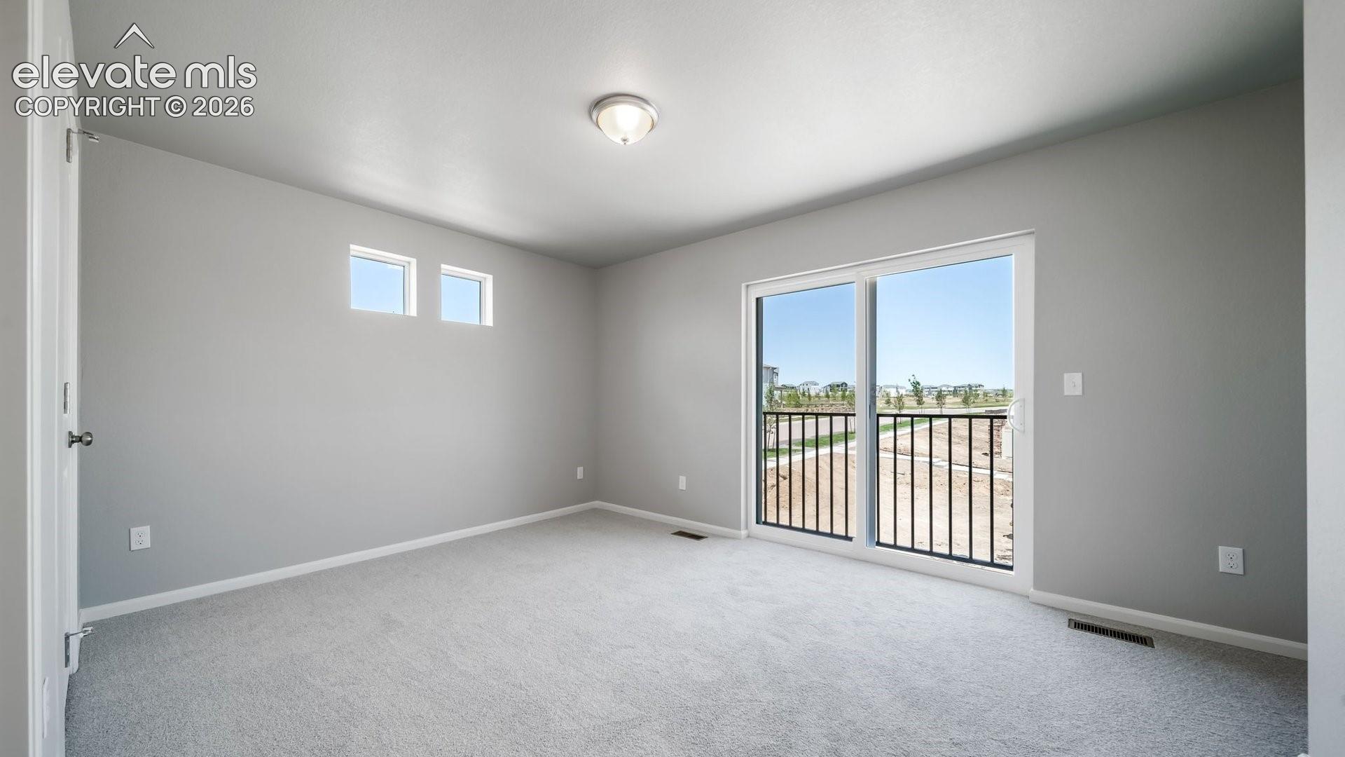 Neutral-toned room featuring neutral carpeting, dual square accent windows, a ceiling-mounted light fixture, and a sliding glass door with an integrated black metal balcony railing
*photos of a model home*