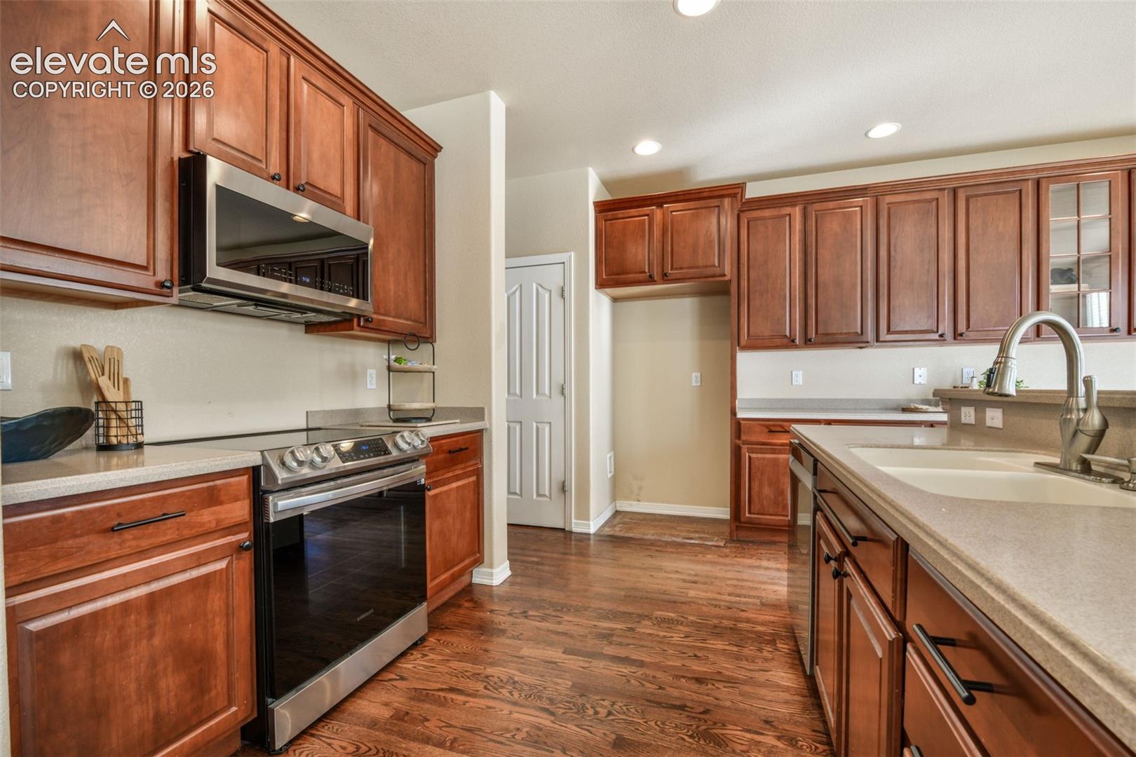 Kitchen featuring wood-finish flooring, rich wood cabinetry, light-toned countertops, a stainless steel range, and an integrated stainless steel microwave