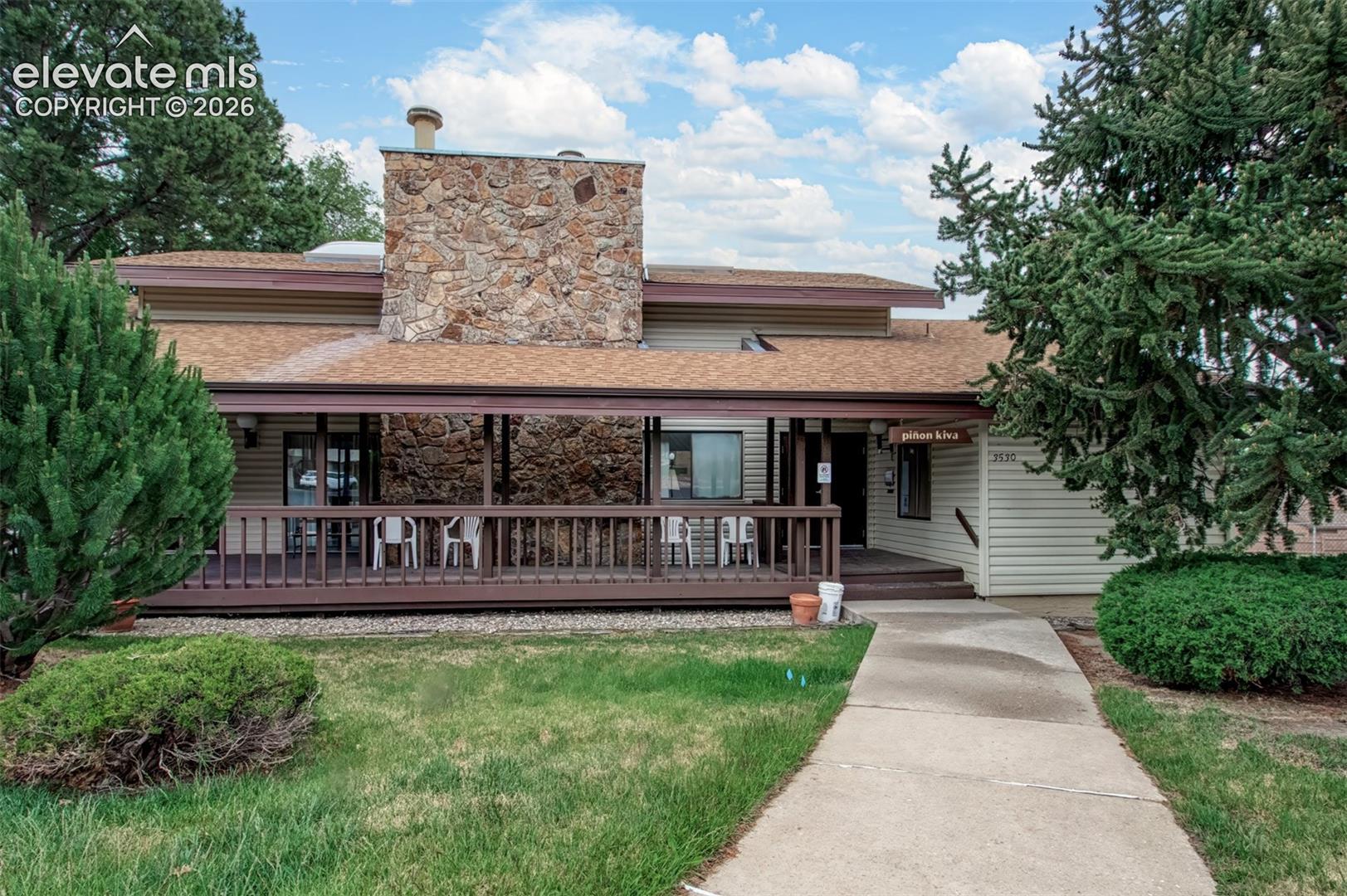 Exterior featuring a prominent stone-faced chimney, horizontal siding, and a covered wood-railing porch