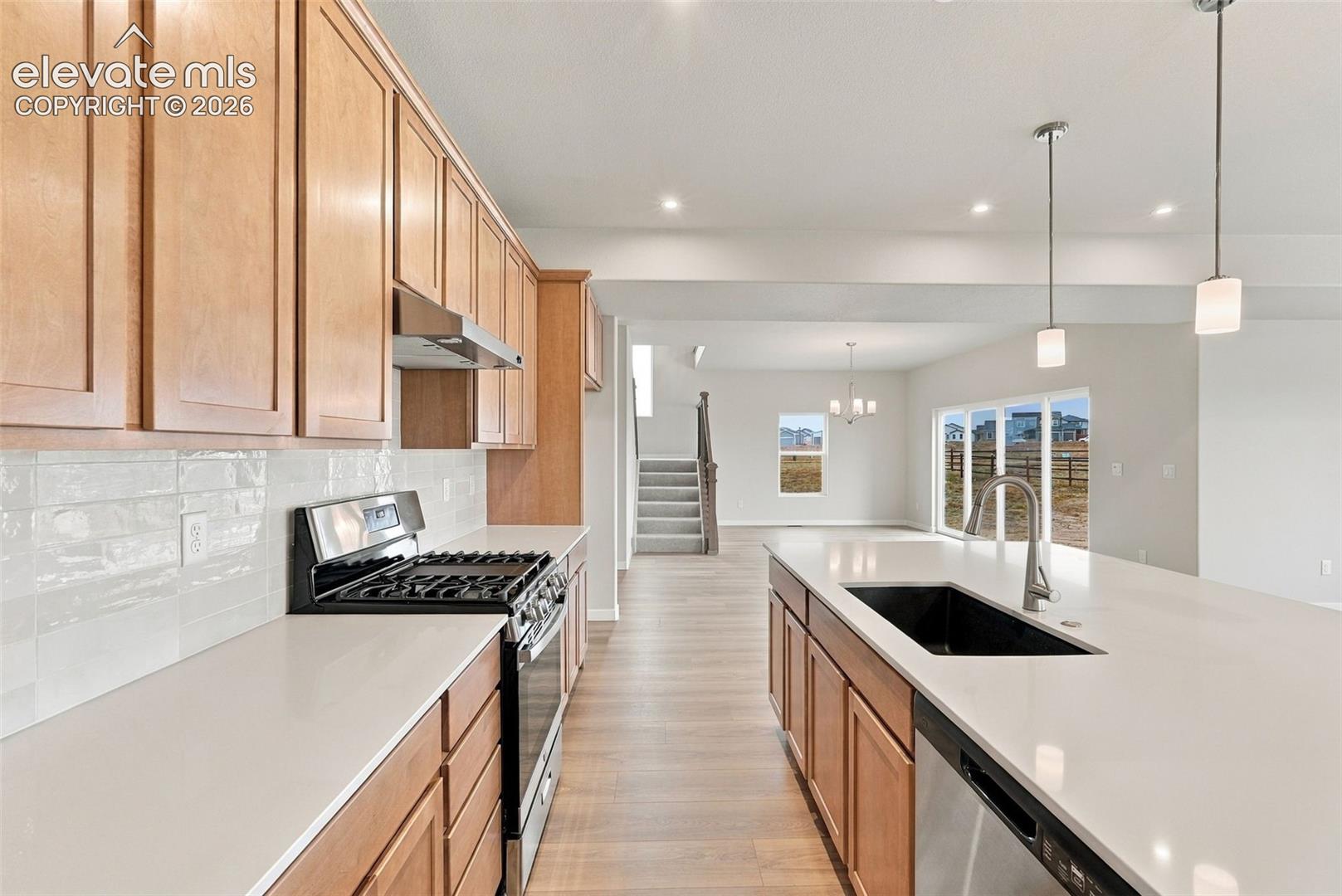 Kitchen featuring light wood cabinetry, quartz countertops, white subway tile backsplash, oversized center island with a stainless steel sink, and wood-finish flooring