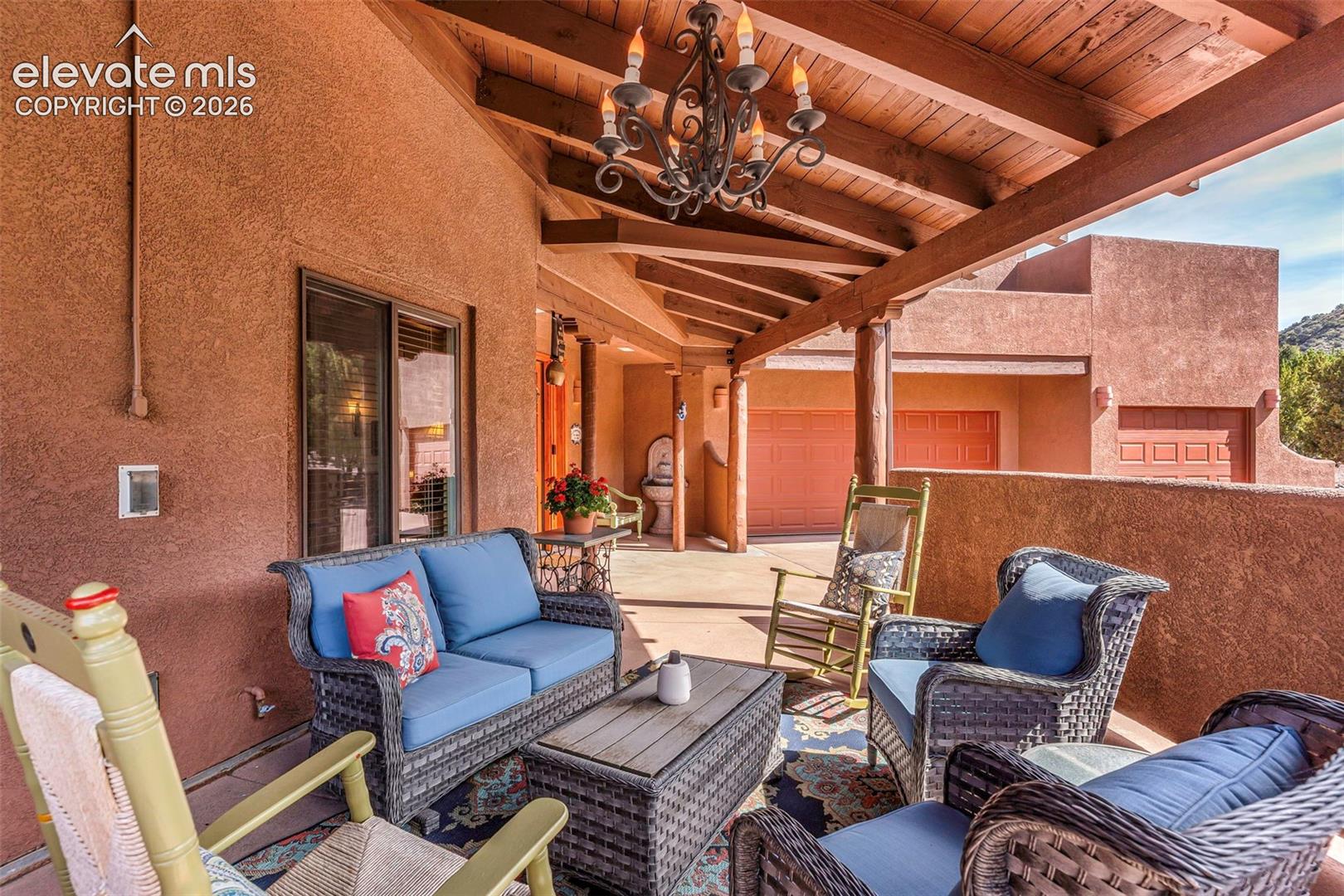 Covered patio featuring exposed wood beam ceilings, textured stucco walls, and a wrought-iron chandelier