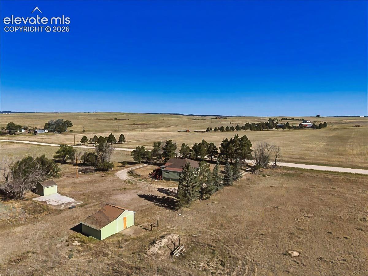Sweeping aerial perspective showcases the property's generous footprint, mature trees, multiple outbuildings, and breathtaking views of the Front Range, Pikes Peak, and the surrounding countryside. Enjoy spectacular Colorado sunsets from this peaceful five-acre setting.