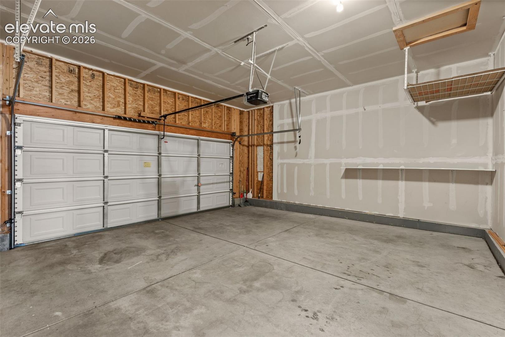 Multi-car garage featuring a sectional overhead door, concrete flooring, built-in wall shelving, and overhead attic access