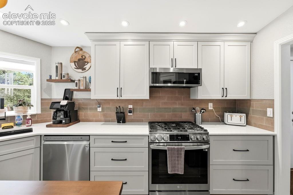 Light-toned cabinetry, white countertops, stainless steel appliances, and a tiled backsplash