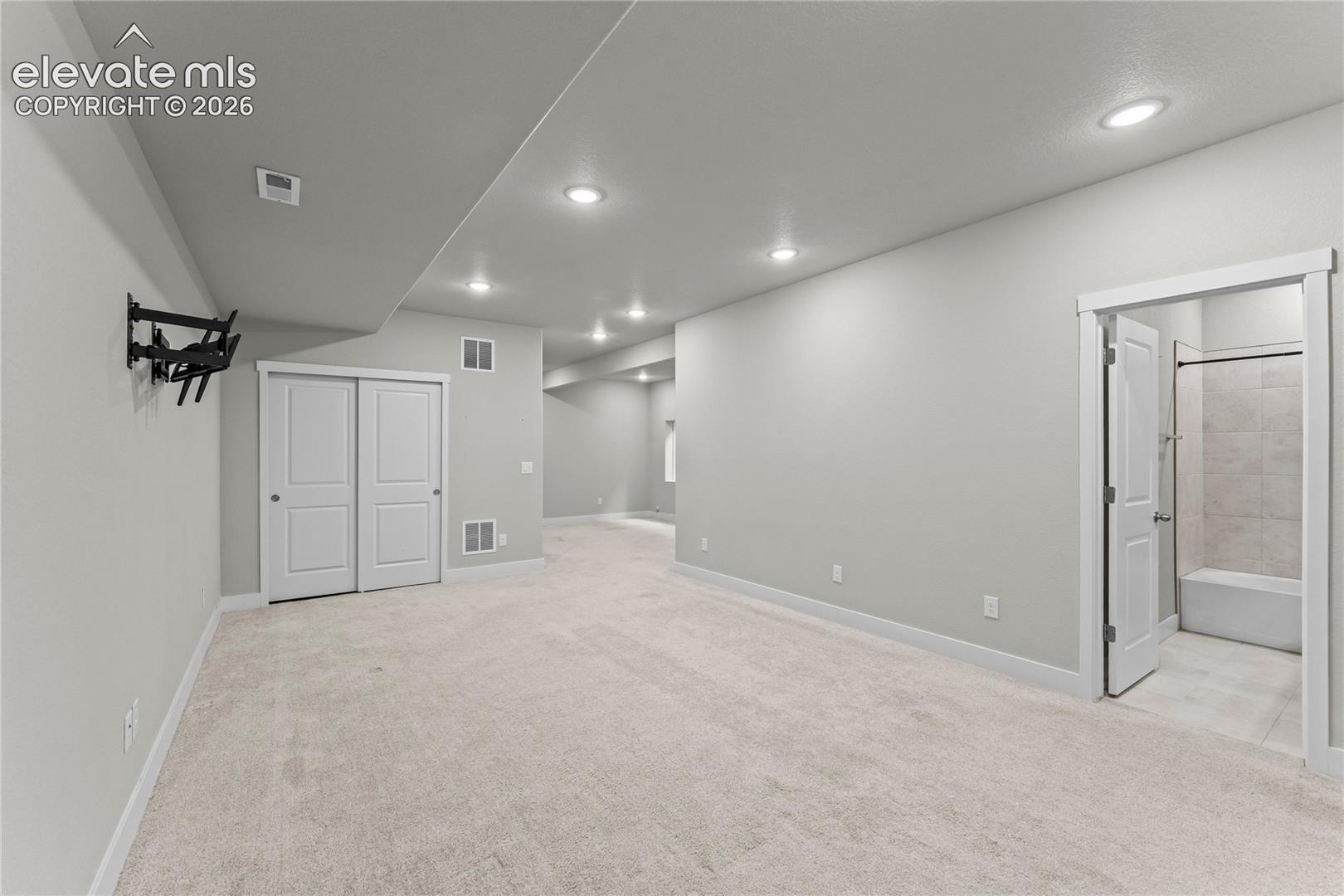 Spacious carpeted room featuring recessed lighting, a closet with sliding doors, and a bathroom with a tiled shower-over-tub combination