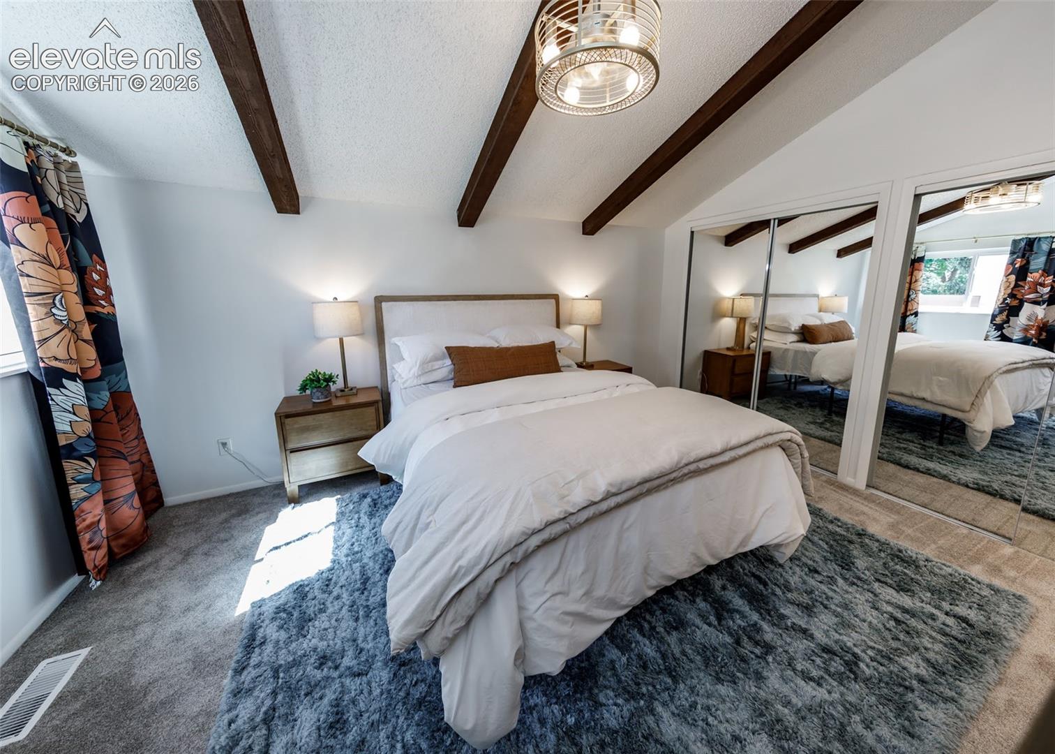 Vaulted ceiling featuring exposed dark wood beams, mirrored closet doors, and drum-style ceiling fixture