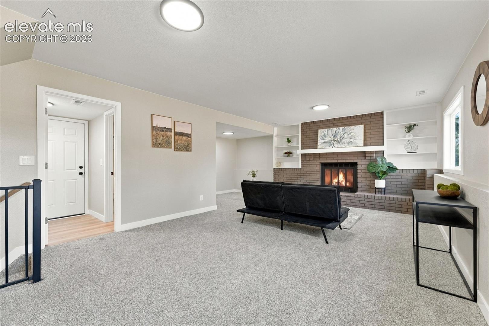 Living area featuring a floor-to-ceiling brown brick fireplace, built-in shelving, carpeted flooring, and flush-mount ceiling lighting