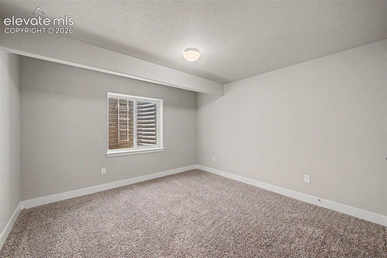 Neutral-toned room featuring a window with security bars, light gray walls, and textured carpet flooring