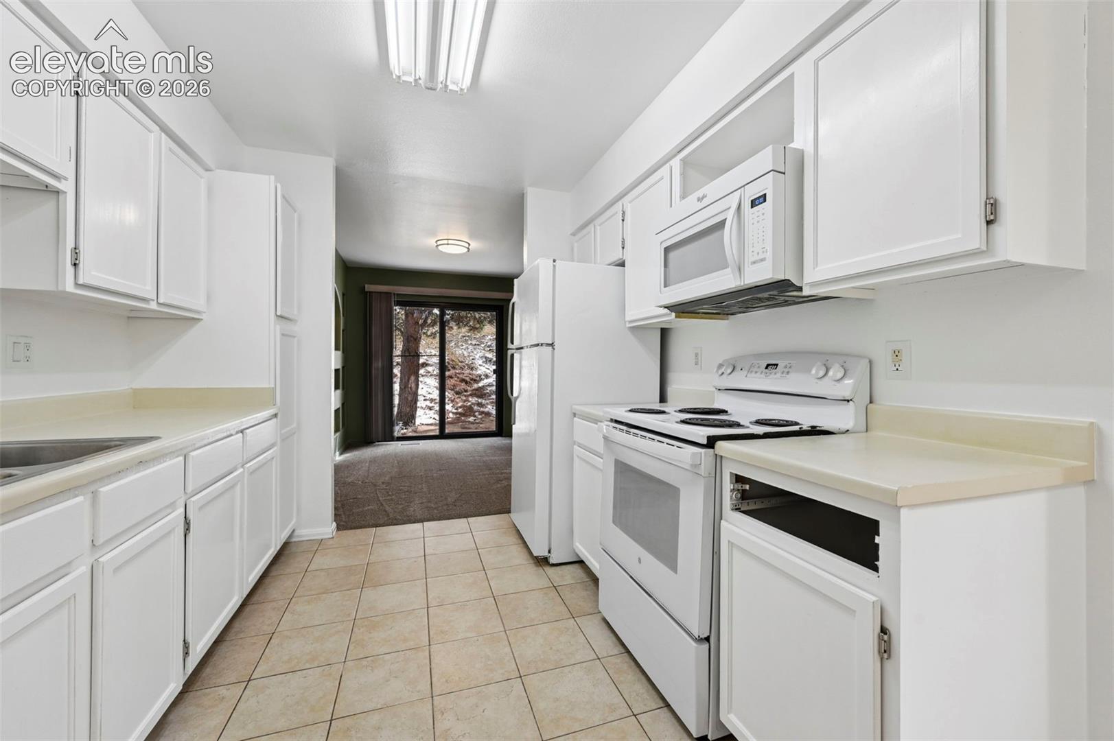 White cabinetry with light-toned countertops, tile flooring, and integrated white appliances