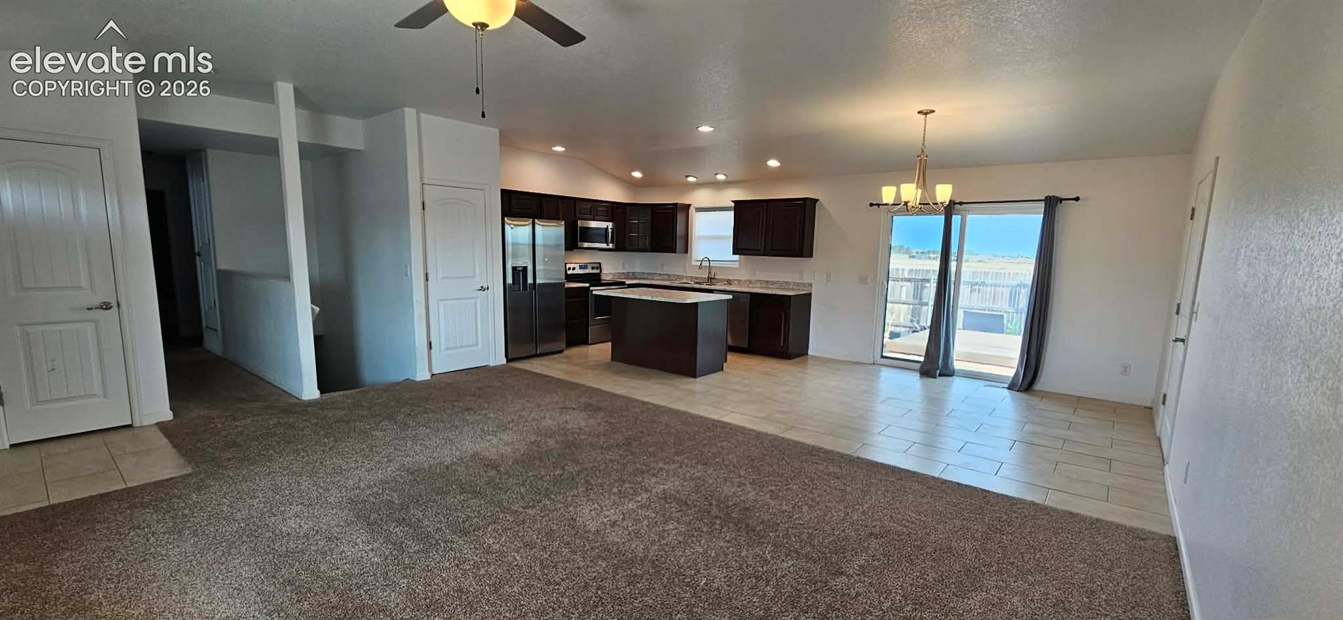 Open concept interior featuring dark-finish cabinetry, a central kitchen island, stainless steel appliances, tile flooring, and sliding glass doors