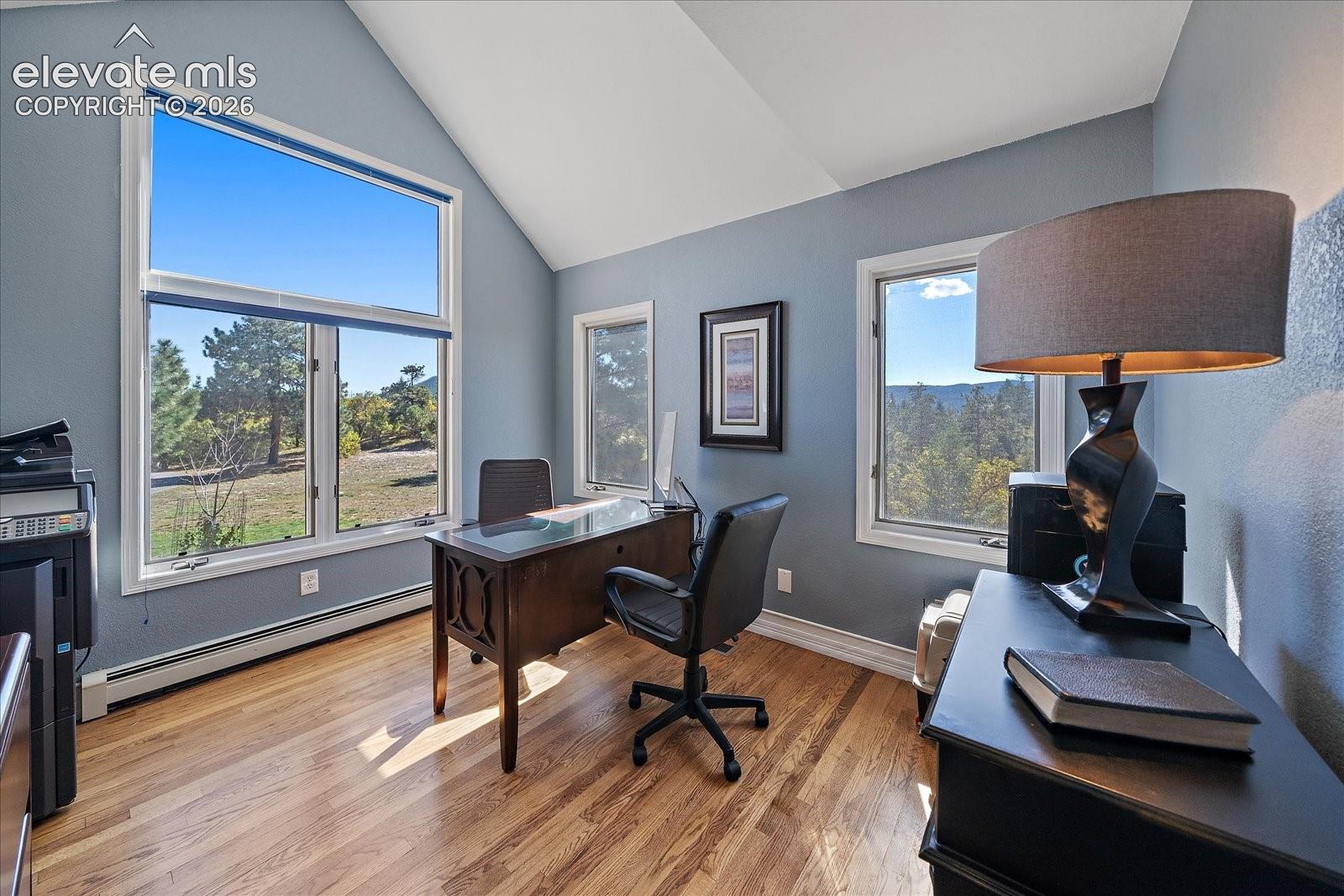 Vaulted ceiling, wood-finish flooring, and expansive windows featuring mountain and woodland scenery