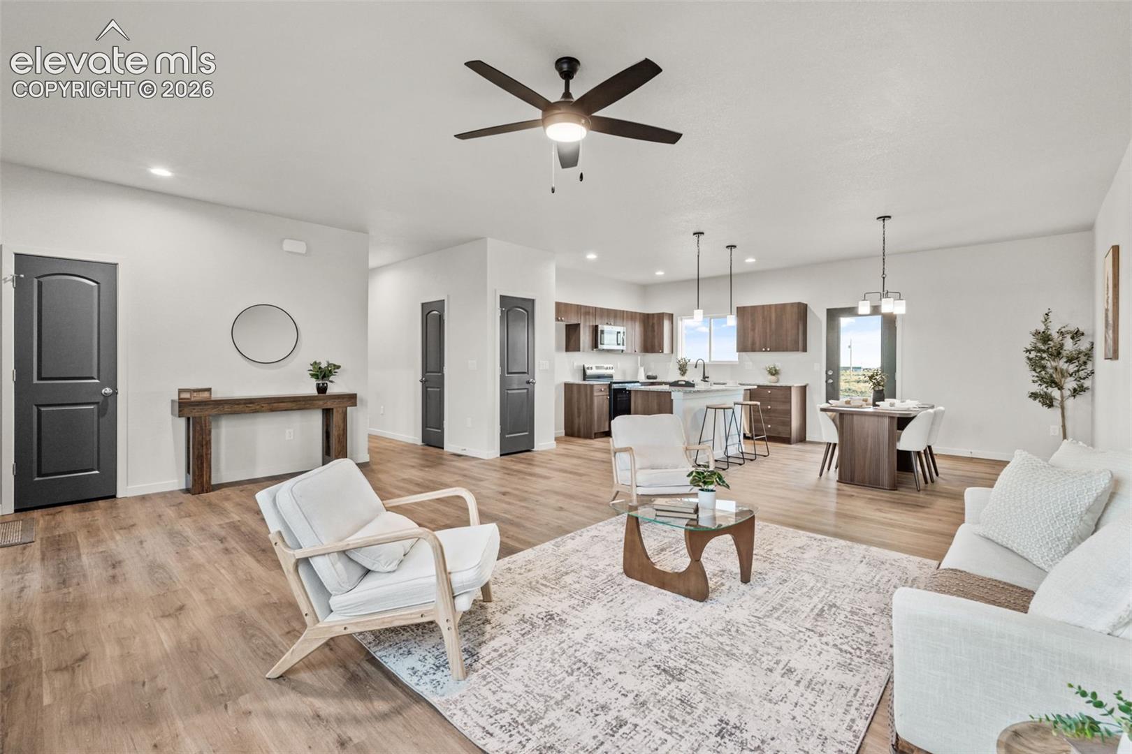 Open-concept interior featuring wood-finish flooring, a kitchen with dark cabinetry and a central island, recessed lighting, and a modern ceiling fan