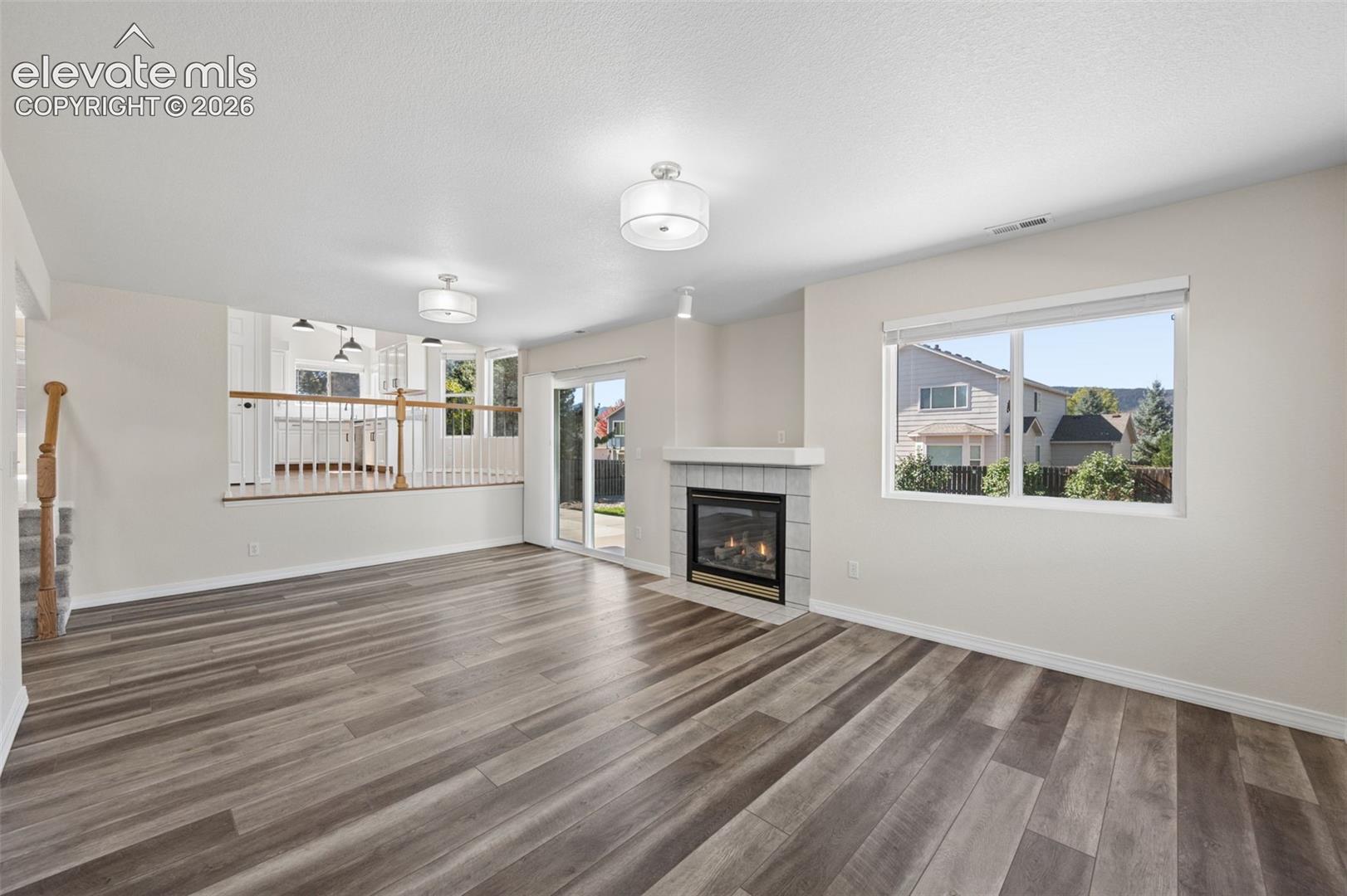 Wood-finish flooring, fireplace with a tile surround and mantel, sliding glass door, recessed lighting, and a partial-height wall with a wooden handrail