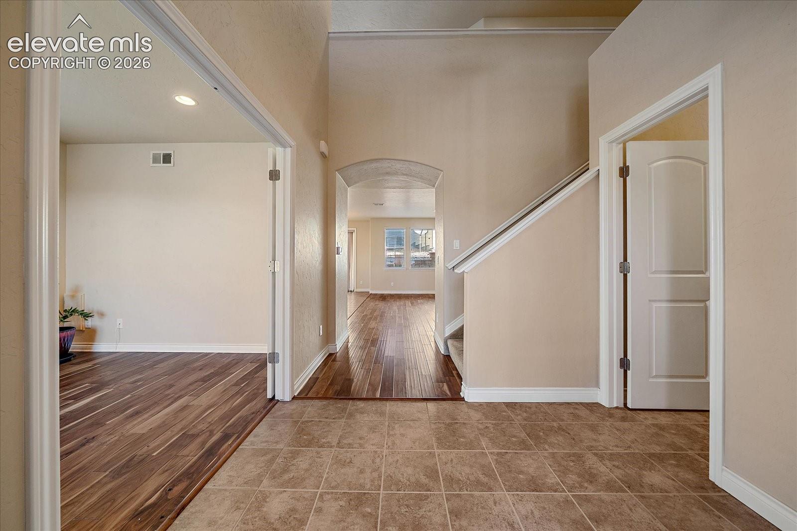 Entryway featuring large-format tile flooring, wood-finish flooring, an arched entryway, high ceilings, and recessed lighting