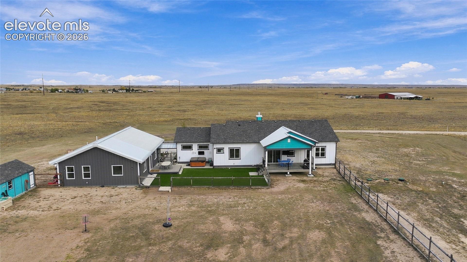 Aerial perspective featuring a multi-structure property with an attached covered porch, a fenced-in turf area, exterior siding, and a dedicated storage building set on acreage