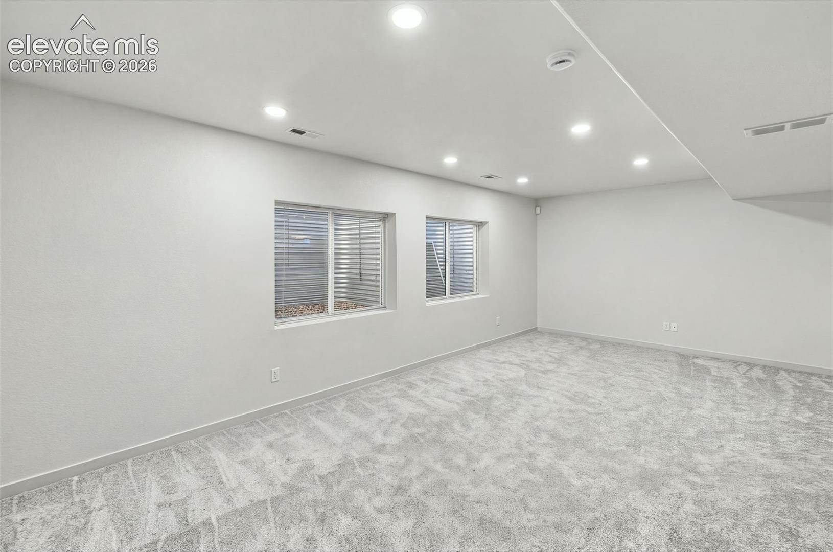 Neutral-toned carpeting, recessed ceiling lighting, and dual egress windows with corrugated metal window wells