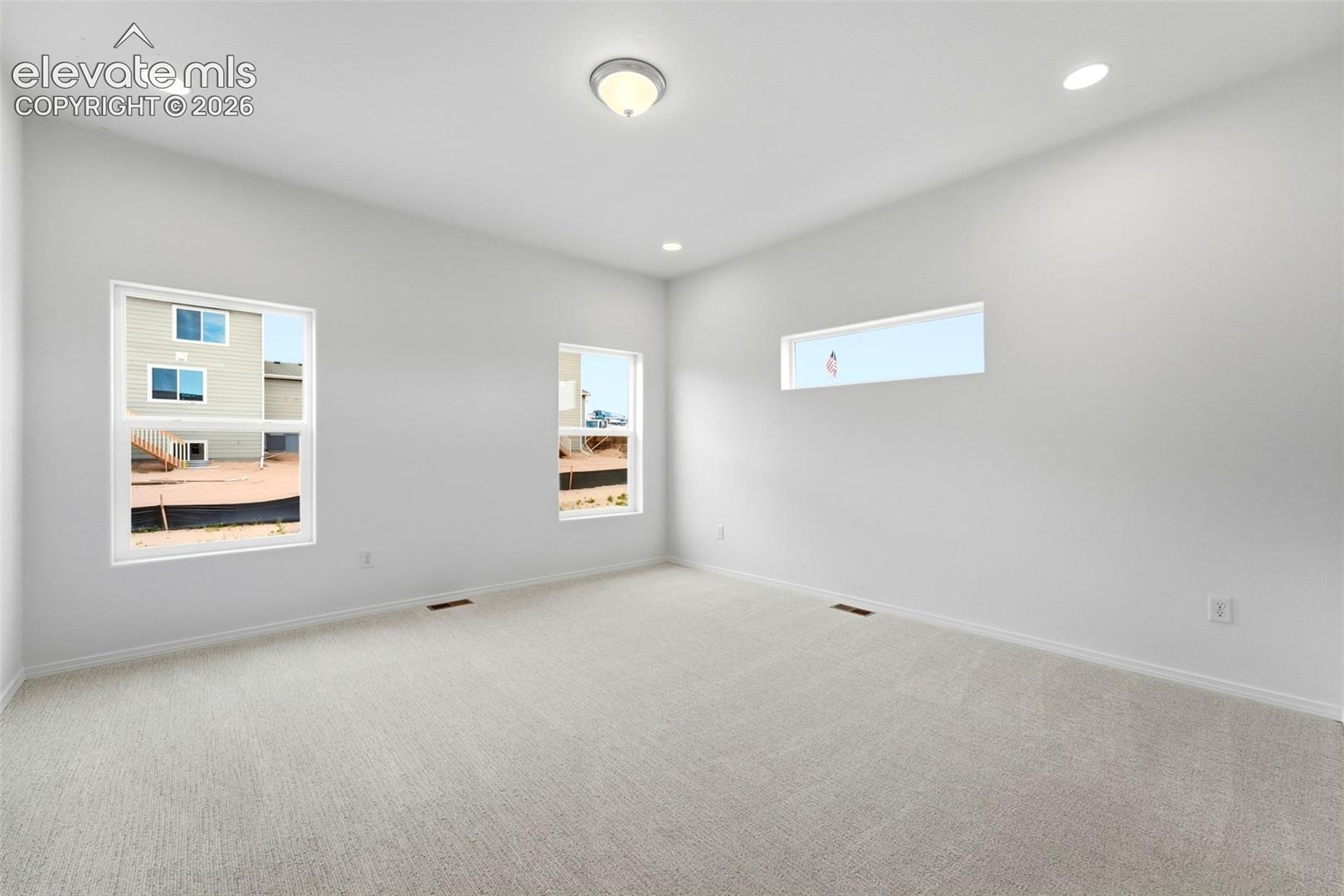 Interior room featuring neutral wall-to-wall carpeting, recessed ceiling lighting, two vertical windows, and a horizontal clerestory window