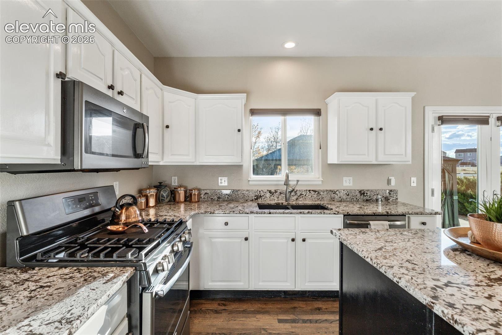 Kitchen featuring white cabinetry, stone countertops, stainless steel appliances, a center island, and wood-finish flooring