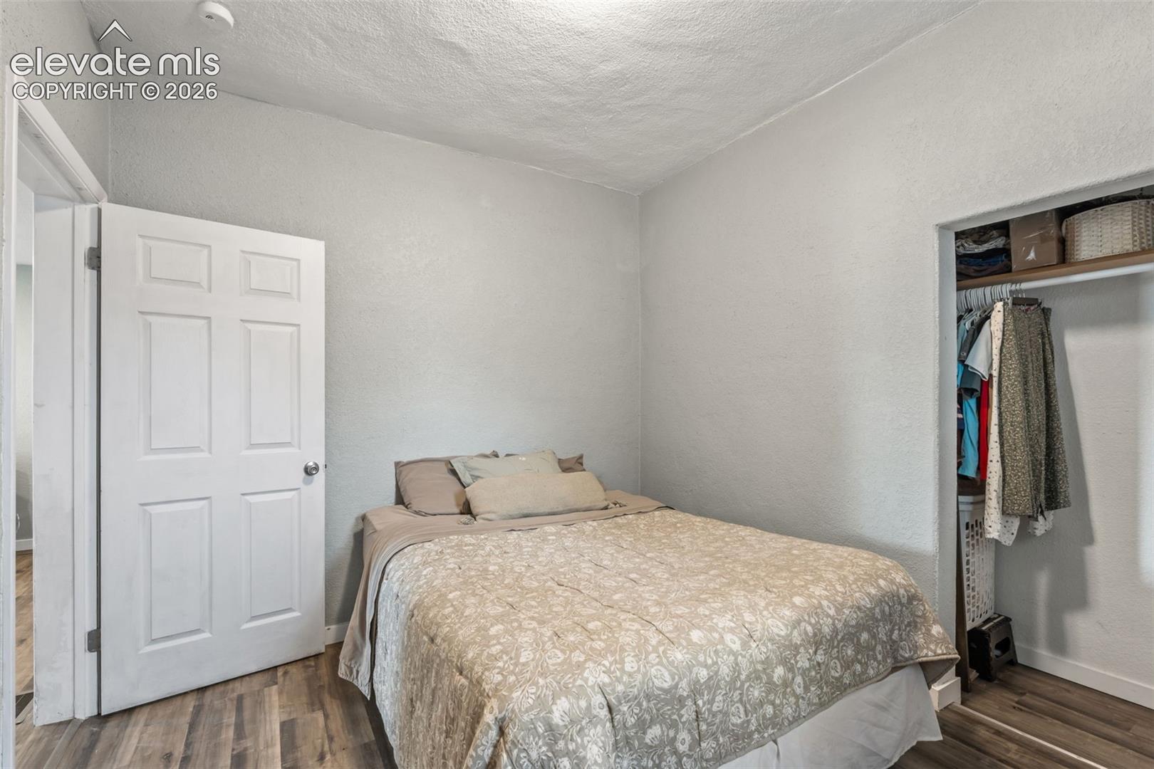 Bedroom featuring wood-finish flooring, a six-panel interior door, and an open closet with built-in shelving and a clothing rod