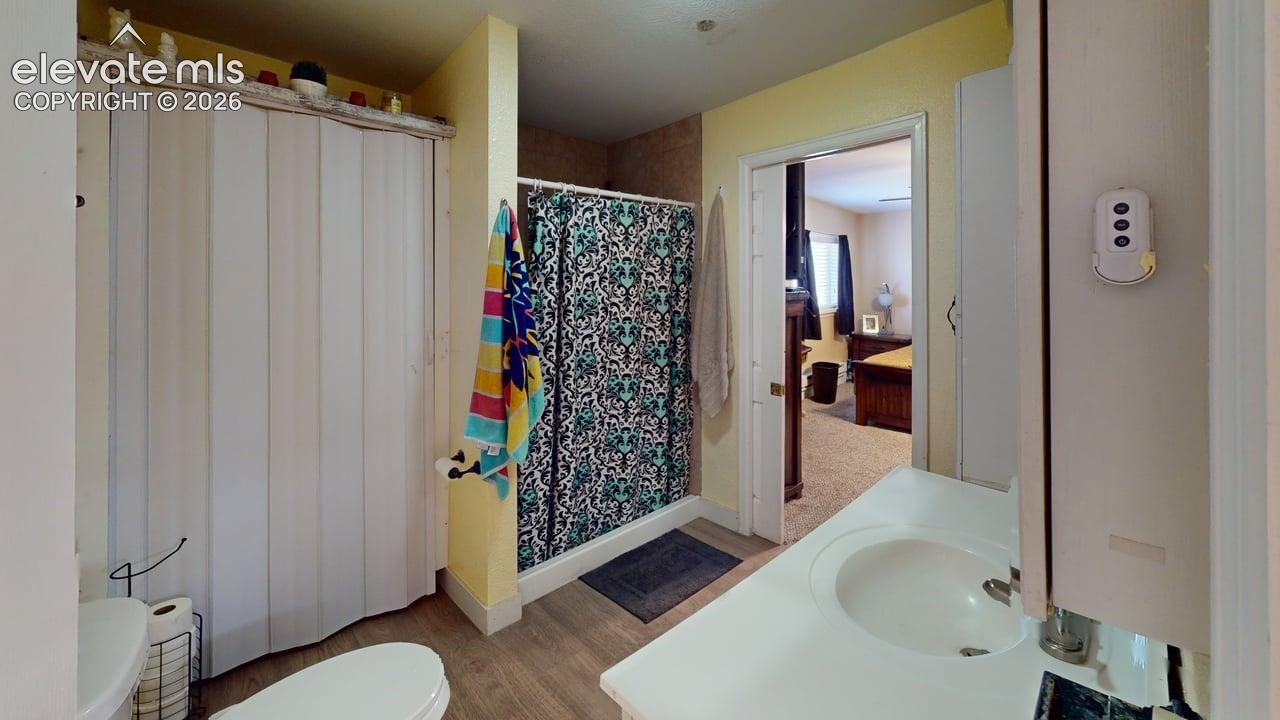 Single vanity with integrated sink, wood-finish flooring, and a shower with a patterned curtain