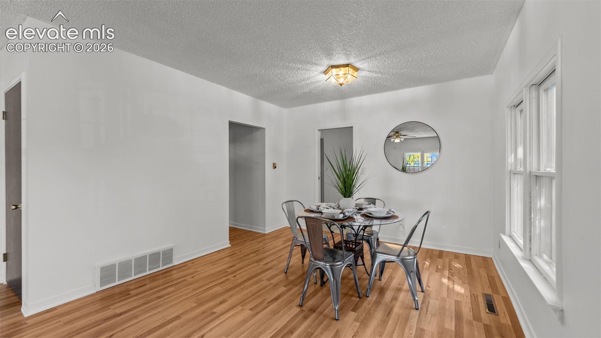 Bright dining area featuring warm wood-finish flooring, white walls, and abundant natural light from large windows