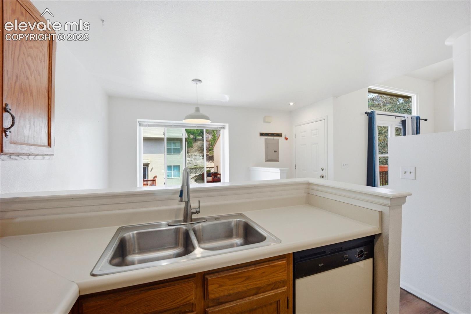 Kitchen featuring a stainless steel double-basin sink, high-arc faucet, solid-surface countertops, wood-finish cabinetry, and a built-in dishwasher