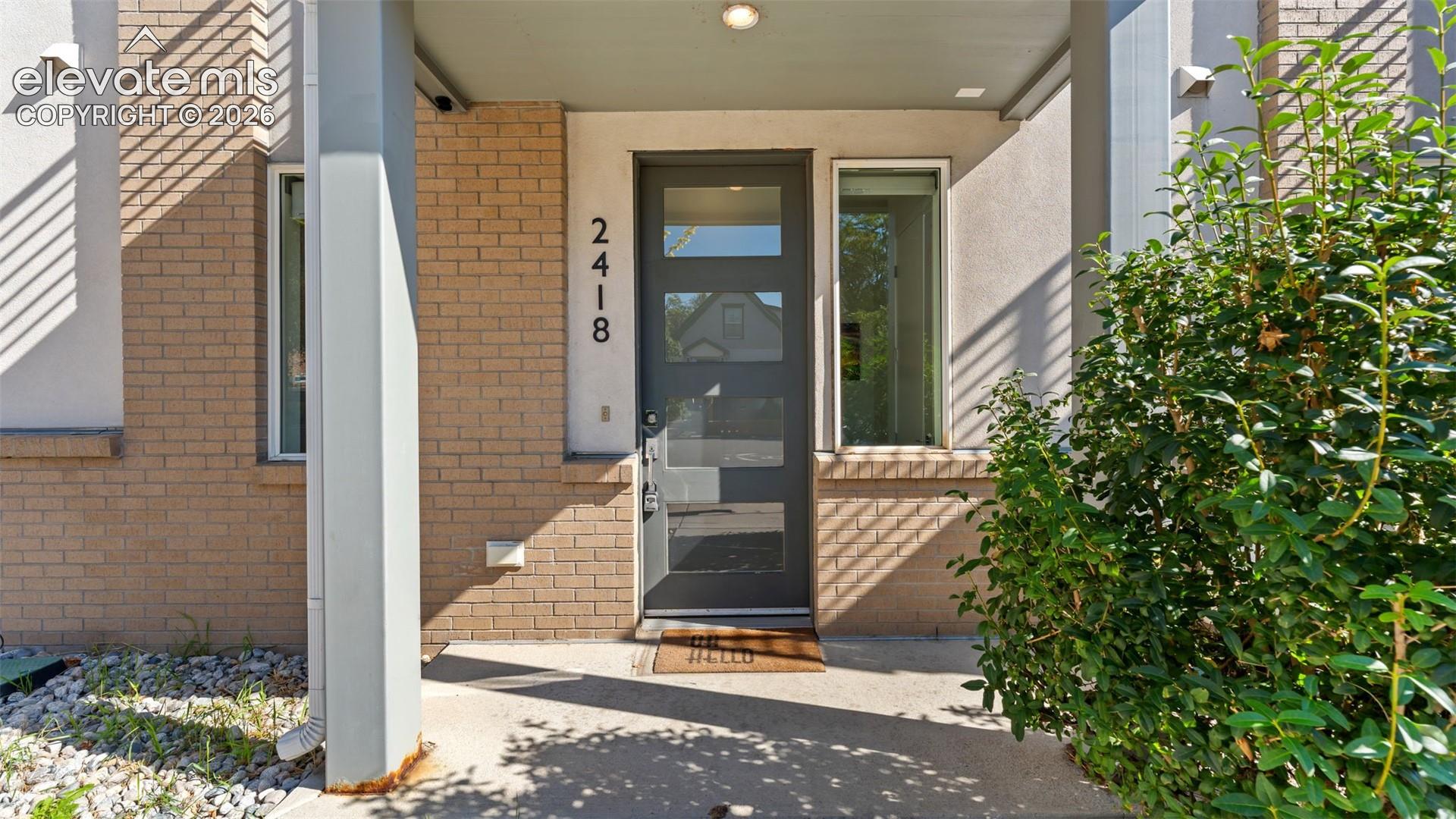 Covered entryway featuring a brick facade, multi-panel front door with glass inserts, and symmetrical windows