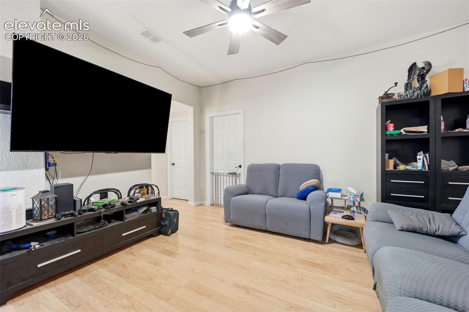 Living area with light wood-finish flooring, light gray walls, and a ceiling fan