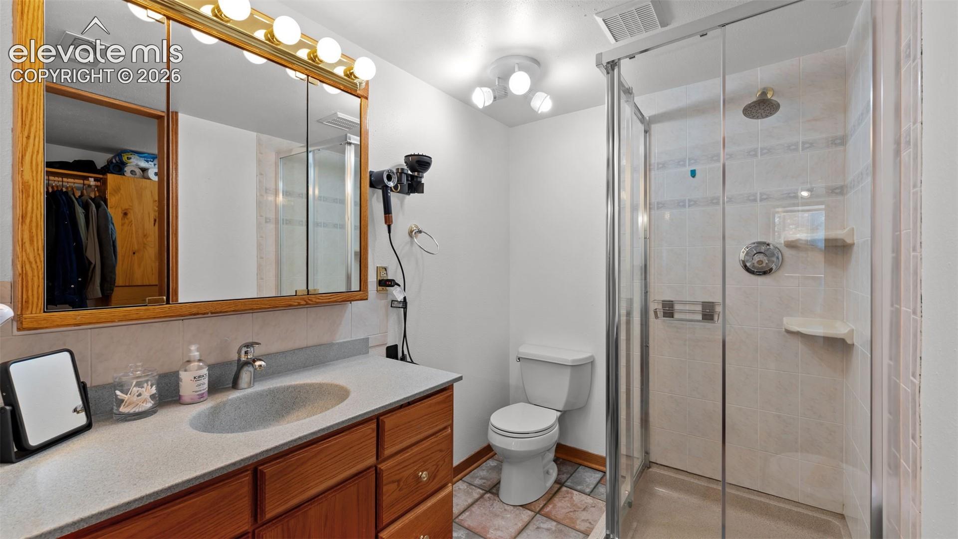 Bathroom featuring a wood-tone vanity with a solid-surface countertop, an integrated sink, a large tri-panel mirrored medicine cabinet, a tiled shower enclosure with glass doors, and ceramic tile flooring