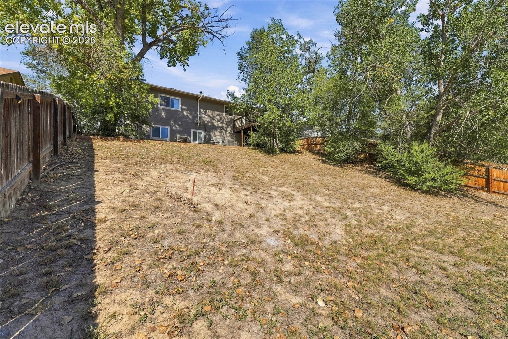 Expansive sloped backyard featuring mature trees, partial fencing, and a two-story exterior with multiple windows