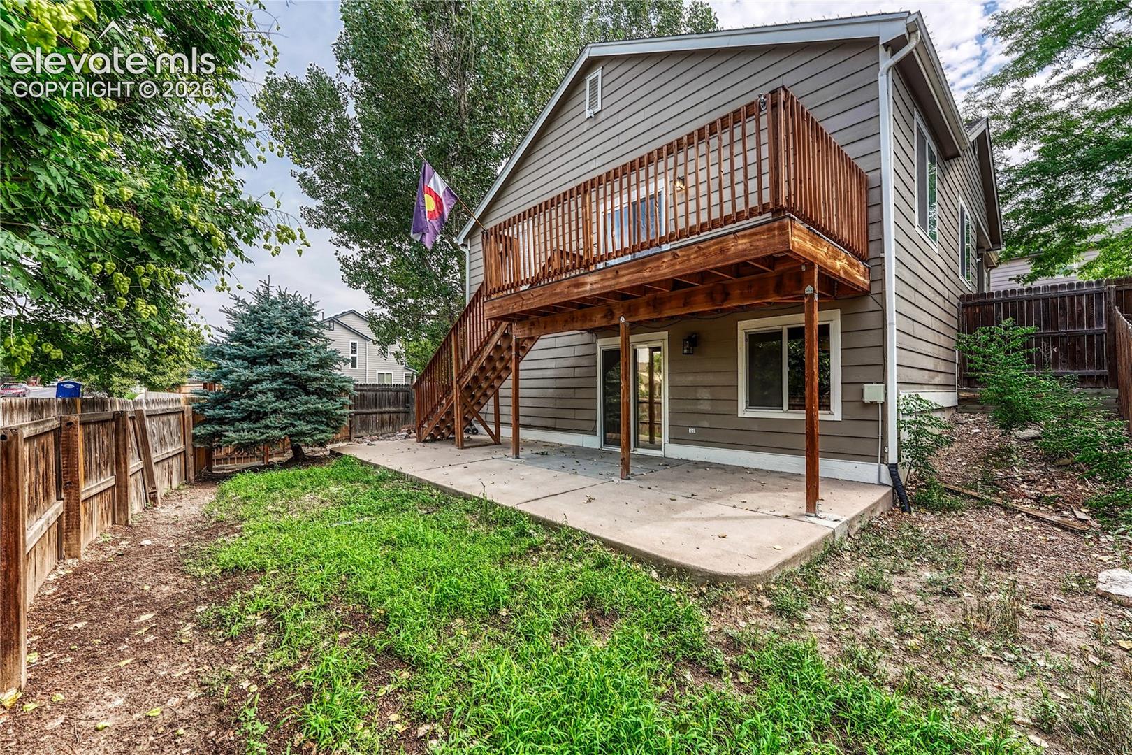 Exterior featuring lap siding, elevated wood deck with stairs, concrete patio, and fenced yard