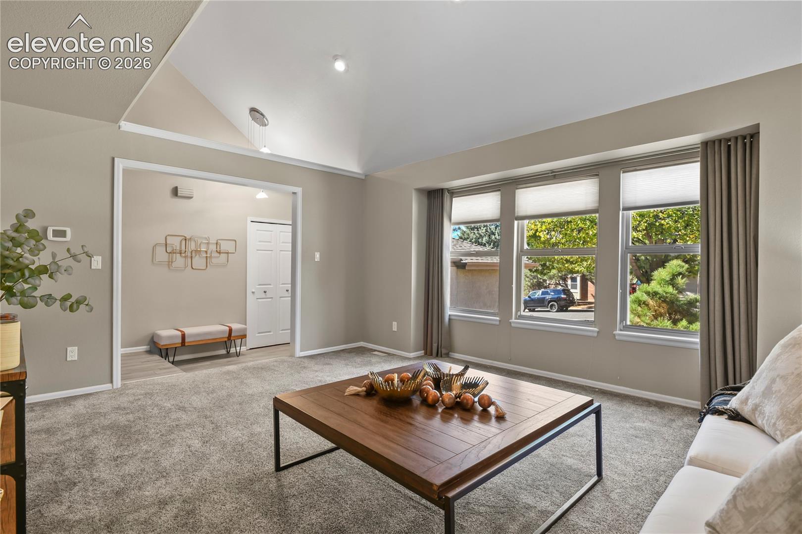 Living area featuring high vaulted ceilings, expansive triple-pane window arrangement with top-down bottom-up shades, and neutral wall tones