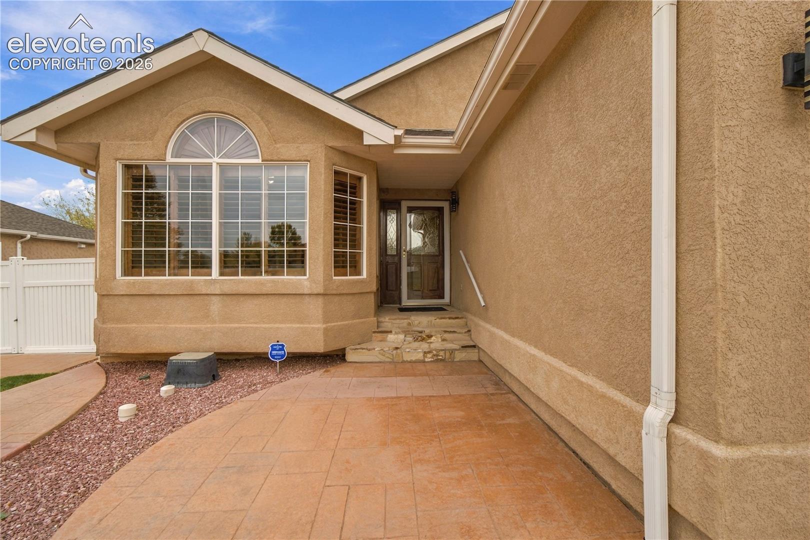 Stucco exterior featuring a gabled roofline, bay window with an arched transom, stone-stepped entry, and a stamped concrete patio